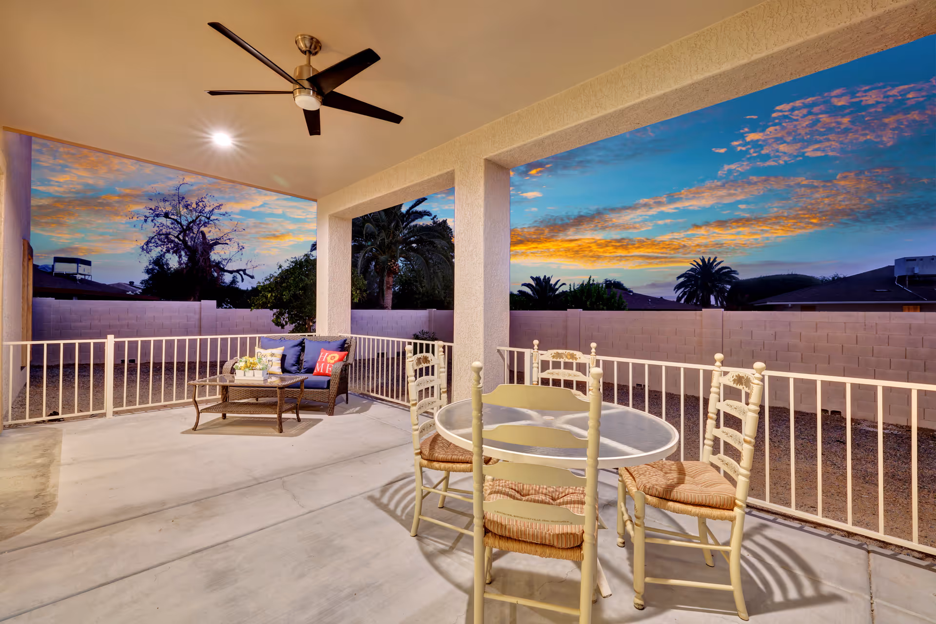 Outdoor patio with seating and sunset sky beyond a white railing