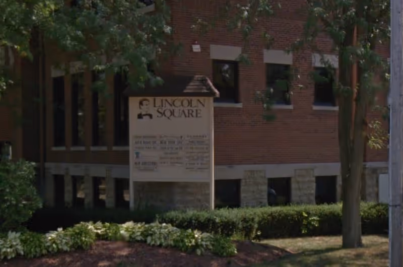 Brick building exterior with a tall sign reading Lincoln Square and surrounding landscaping.