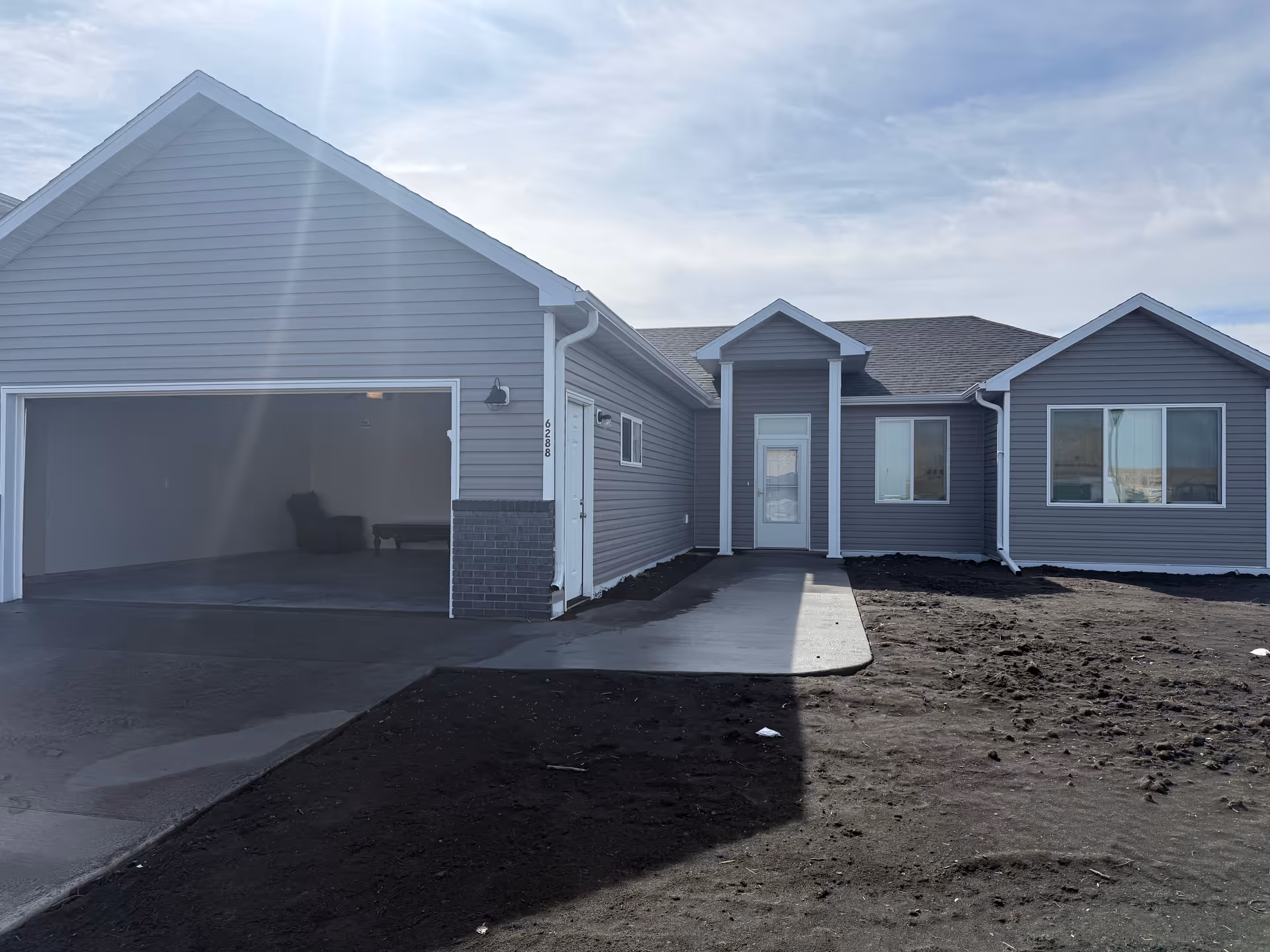 Blue-gray ranch-style home with an open garage and front walkway.