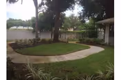 A curved concrete walkway winds through a grassy courtyard with trees beside a building.