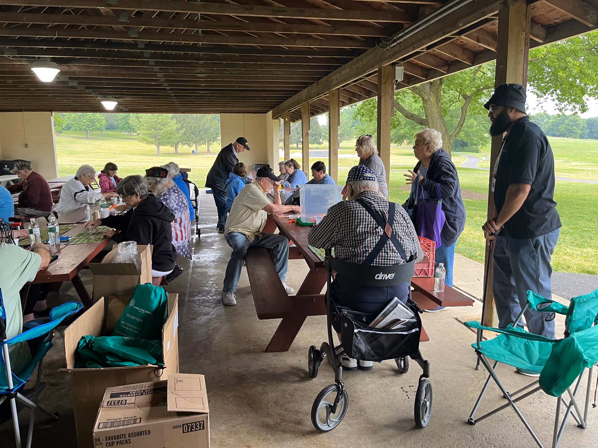Group of seniors gathered at picnic tables under a shaded pavilion in a park.