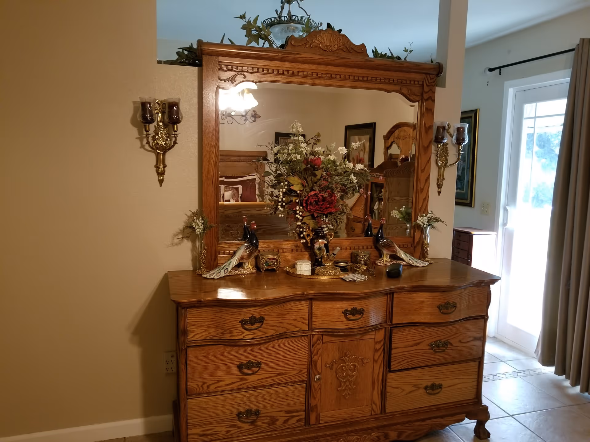 Oak dresser with ornate mirror and floral arrangement in a well-lit living room.