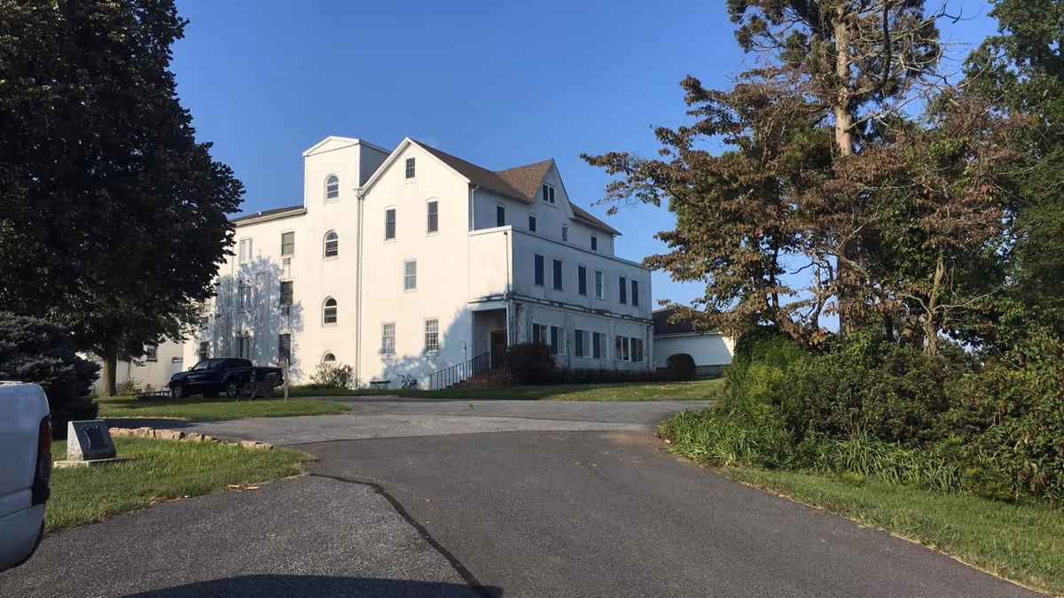 Exterior view of a large white senior living facility along a curved driveway.