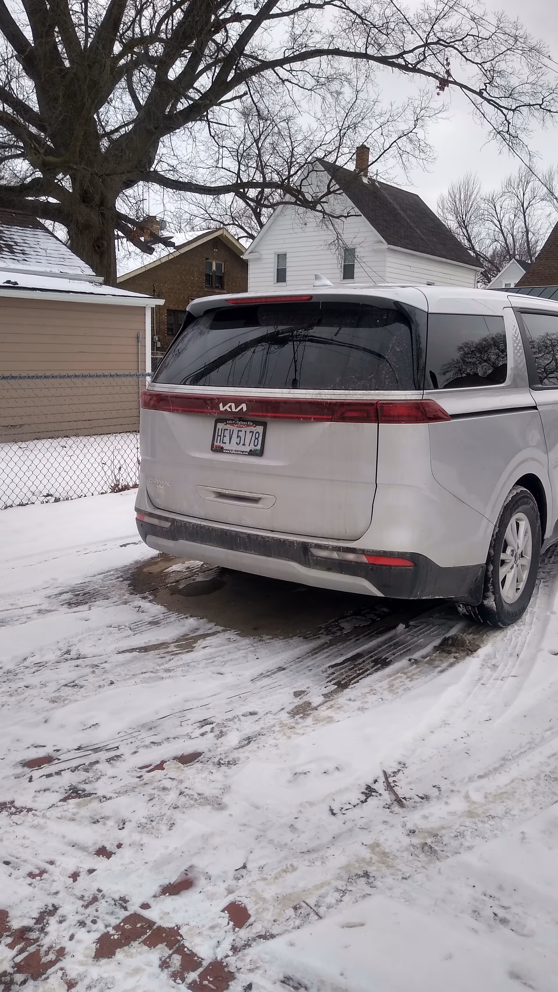 White minivan parked on a snowy residential driveway with houses in the background.