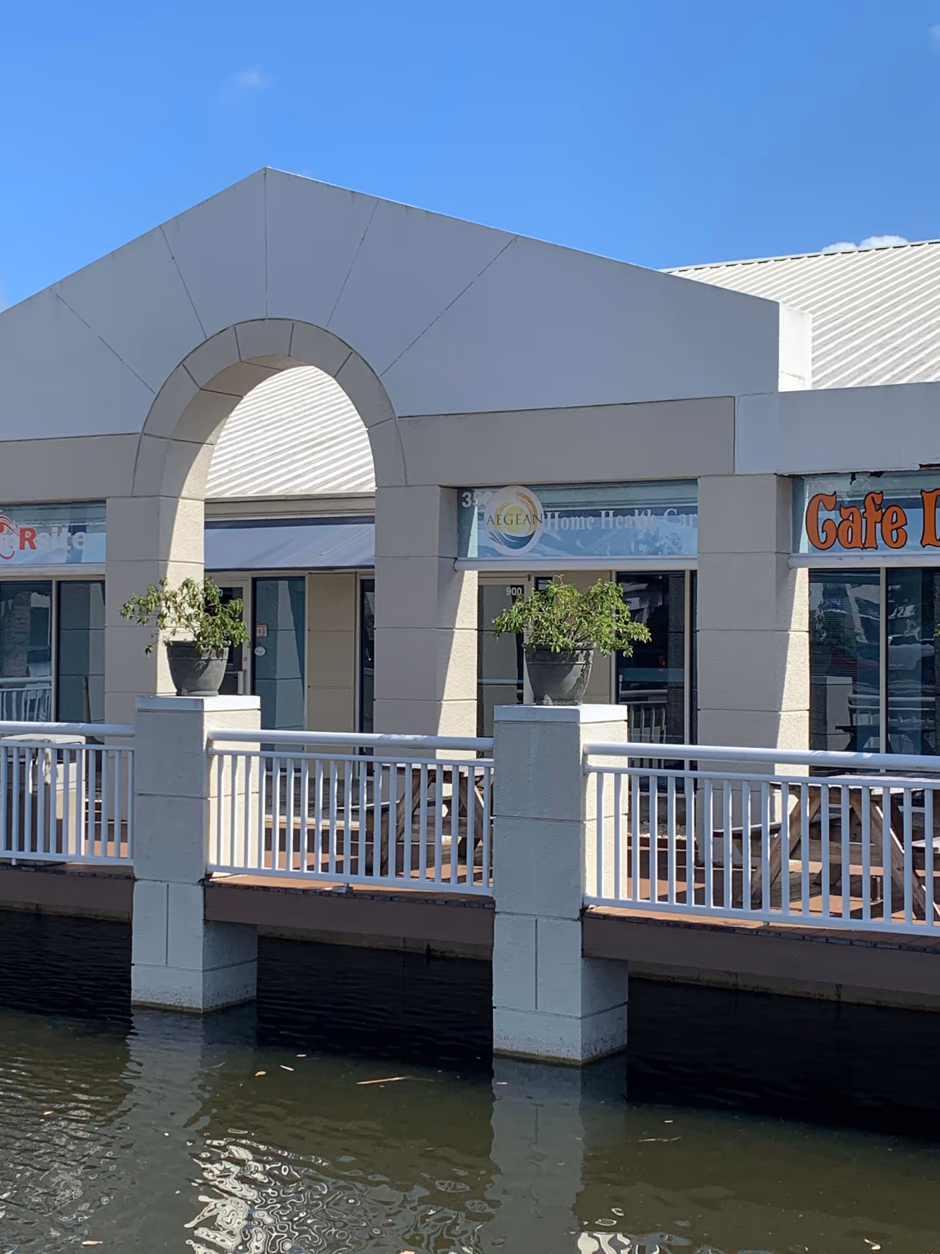 Exterior view of a waterfront building with arched entrance and potted plants.