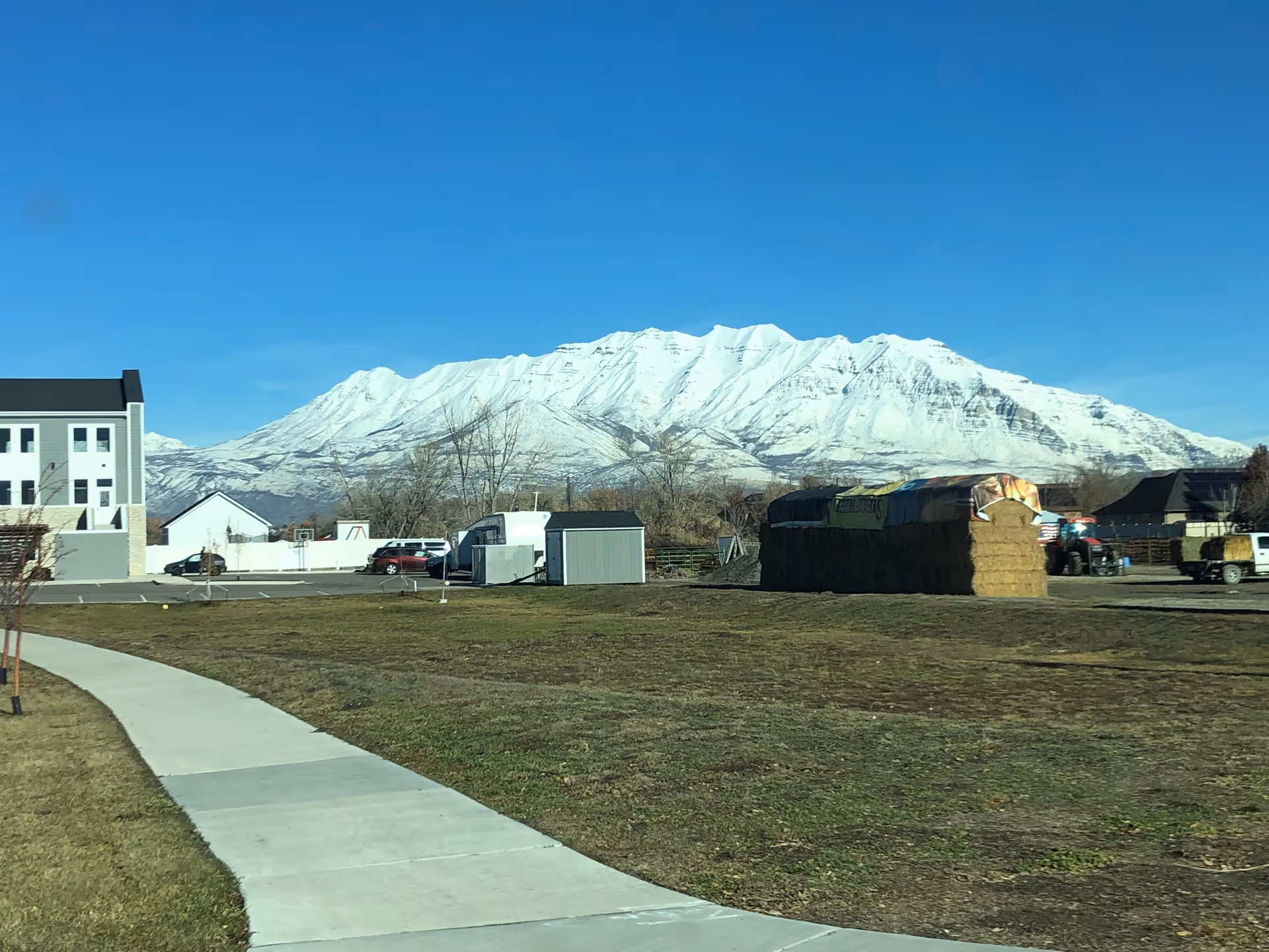 Exterior view of BeeHive Homes of Orem, with snow-capped mountains, curved sidewalk, and hay bales.