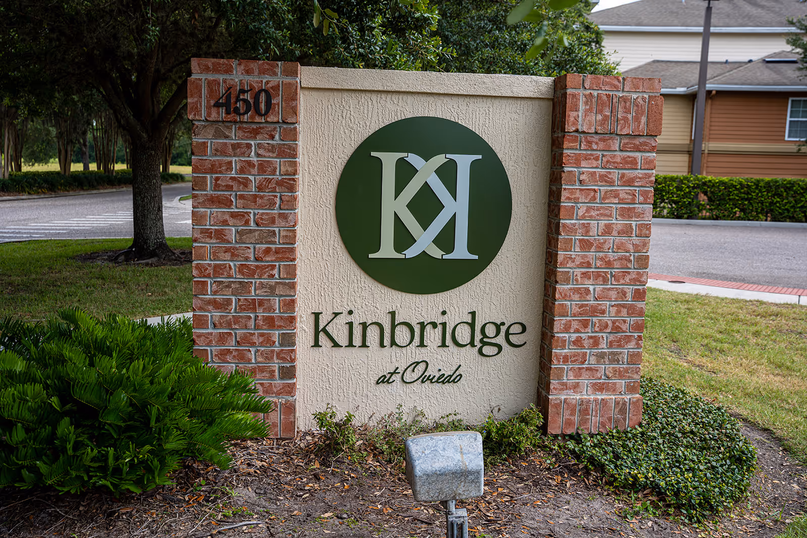 Exterior brick sign reads Kinbridge at Oviedo with a green circular logo and landscaping.