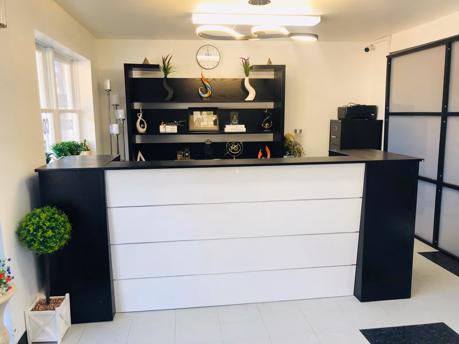 Modern reception desk in a bright lobby with shelves, decor, and potted plants.