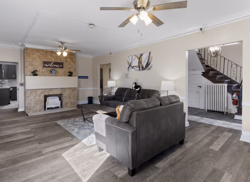 Spacious senior living lounge with a dark gray sectional, coffee table, fireplace, and staircase.