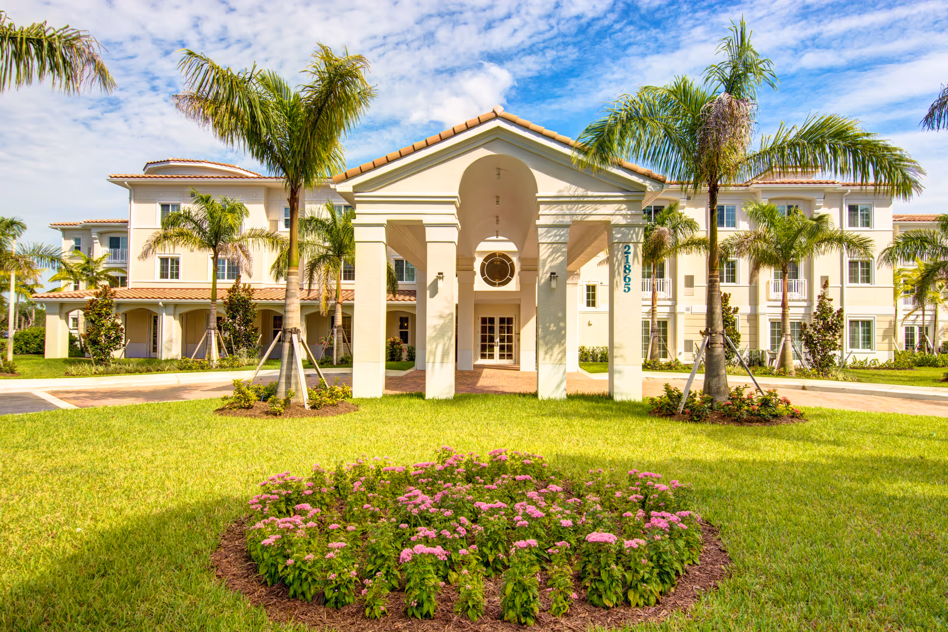 Front view of The Meridian at Boca Raton, a Mediterranean-style senior living building with palm trees.