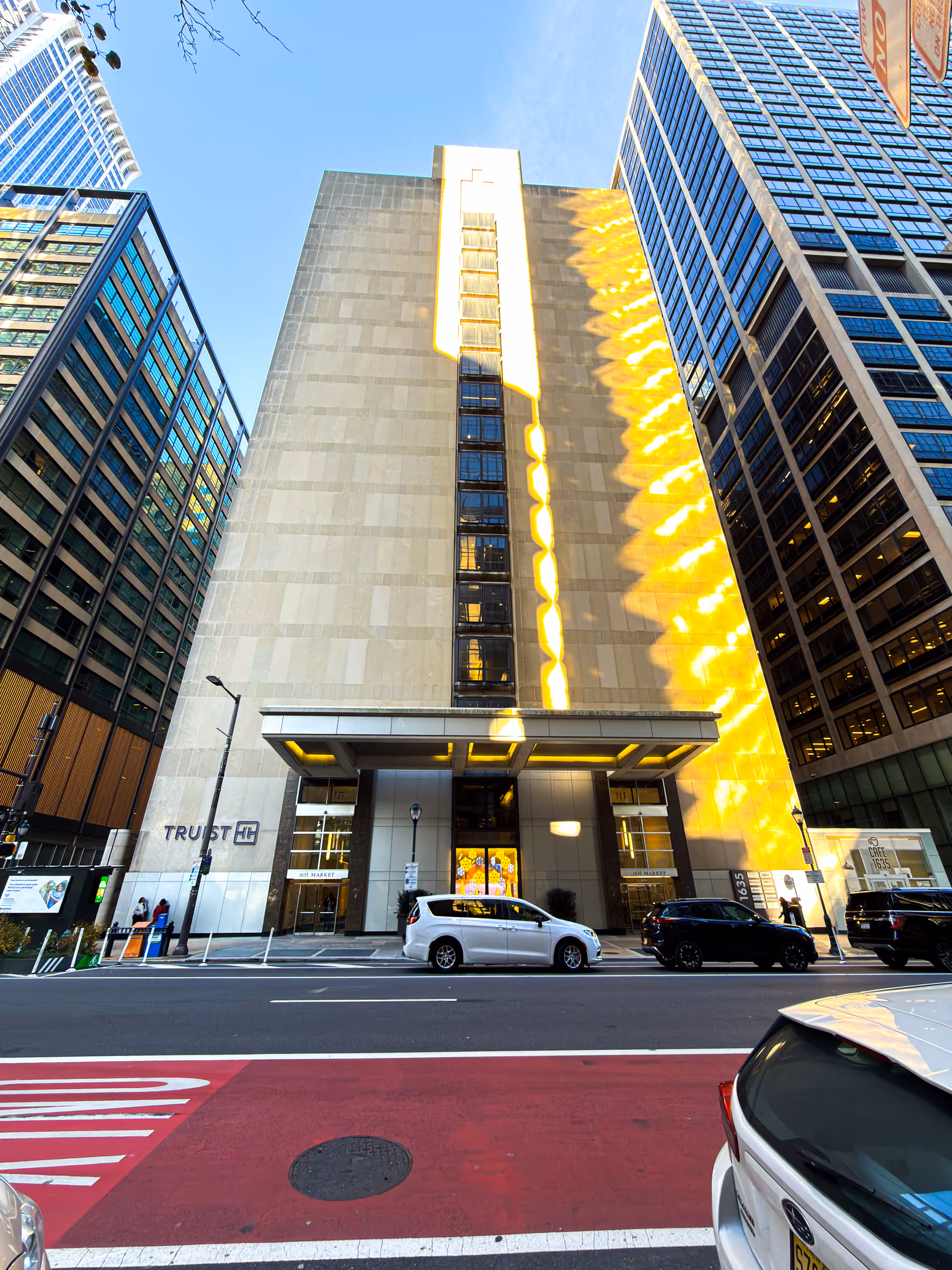 Tall modern building facade photographed from the street with cars parked along the curb.