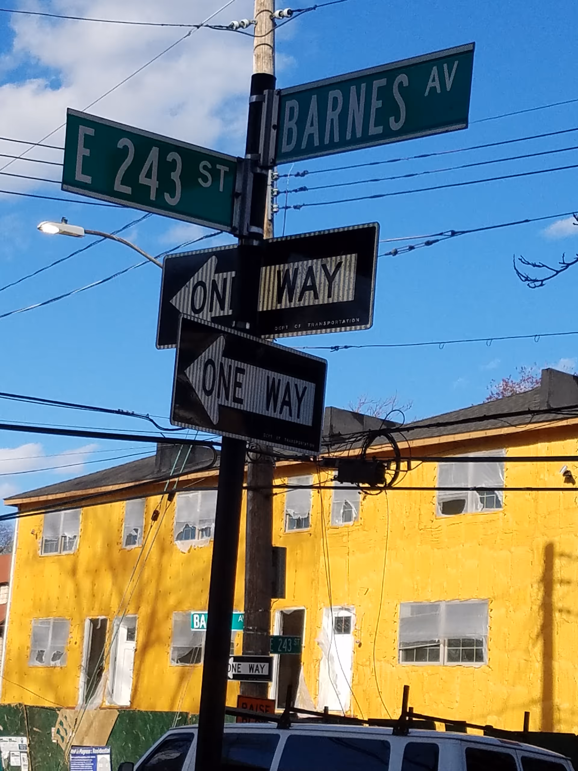 Intersection of E 243 St and Barnes Av with one-way signs near a yellow building