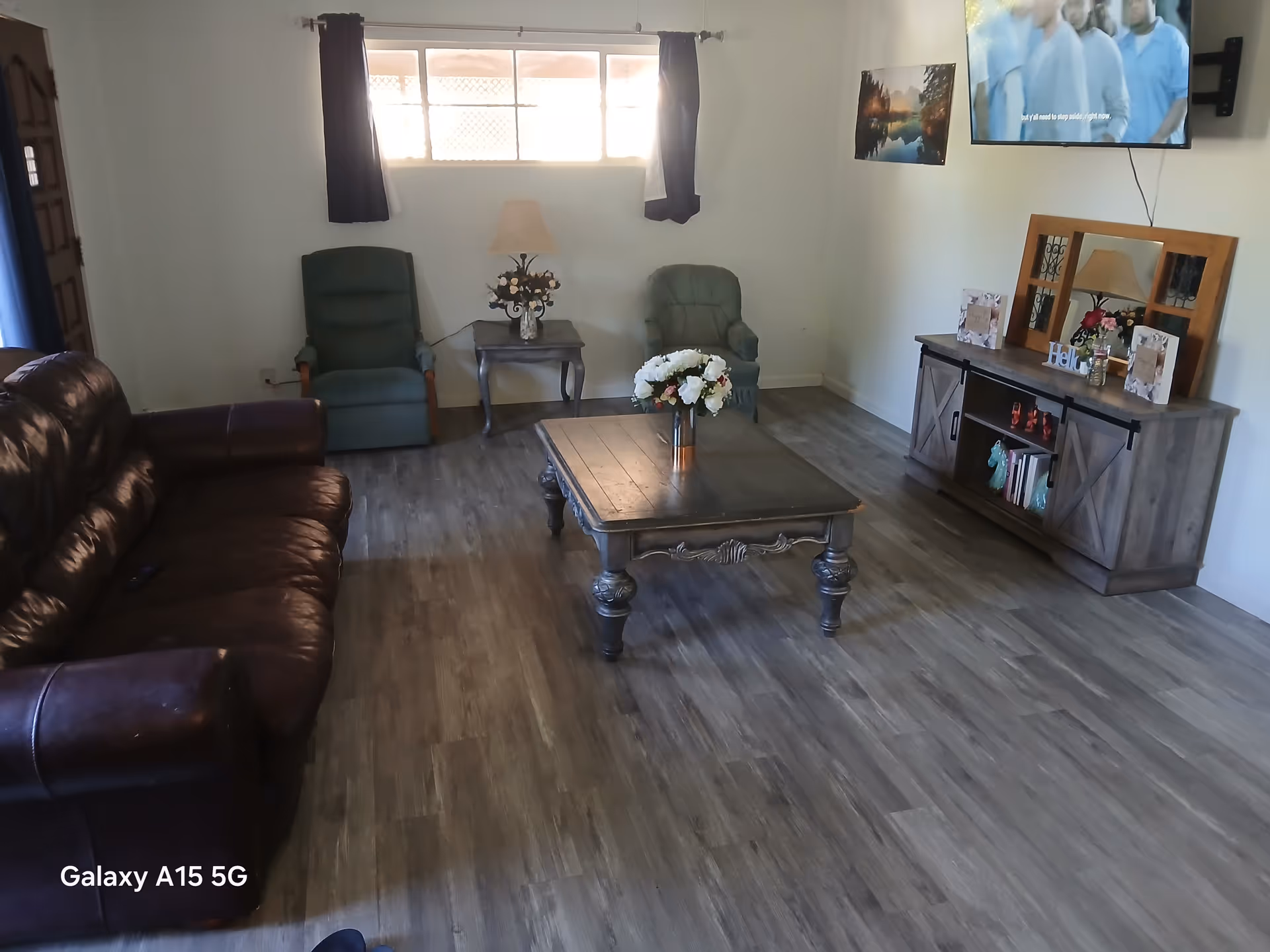 Warm living room with leather sofa, green chairs, coffee table, and mounted TV.
