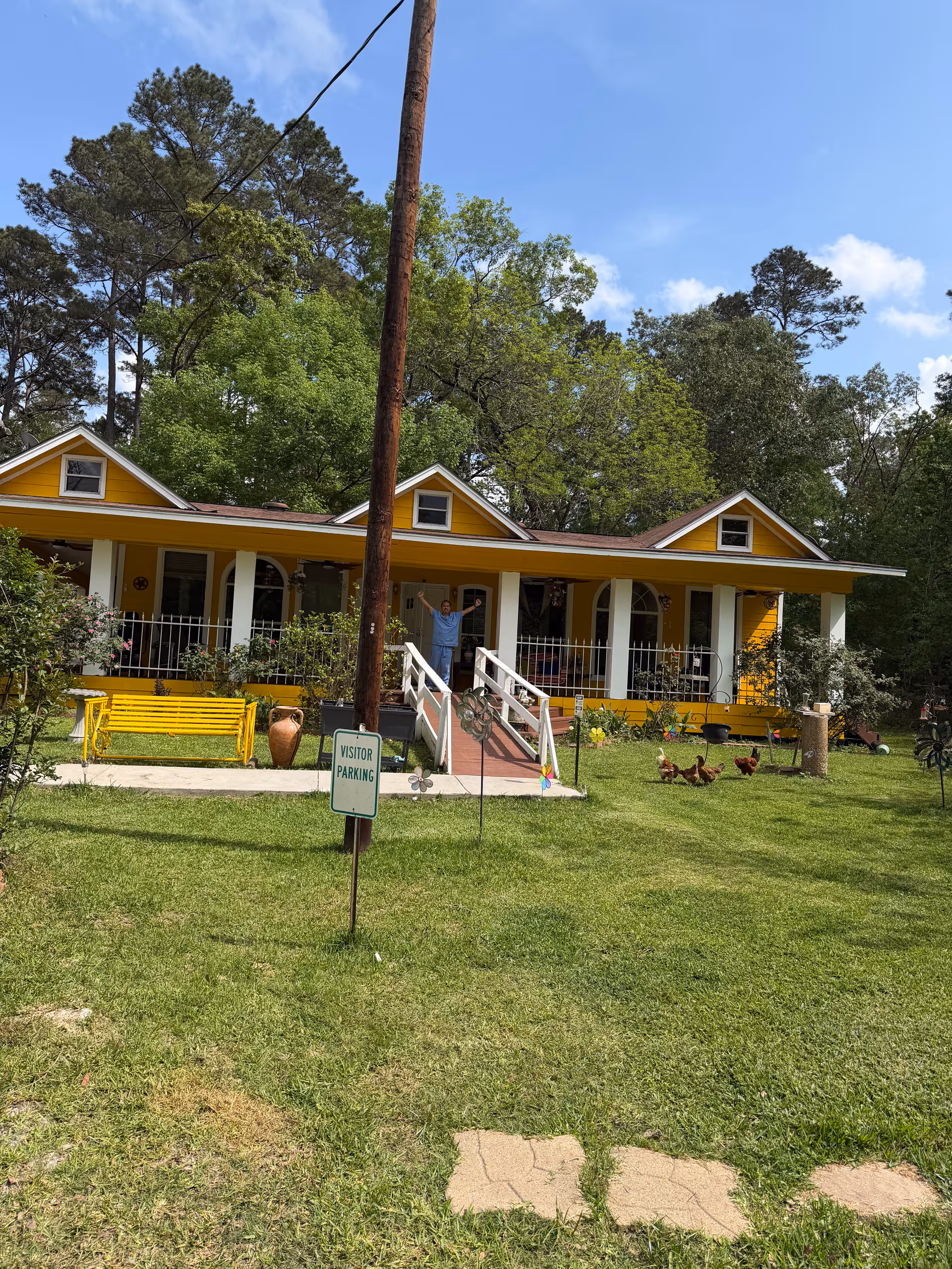 Bright yellow residential care facility with a front porch, ramp, and visitor parking sign.