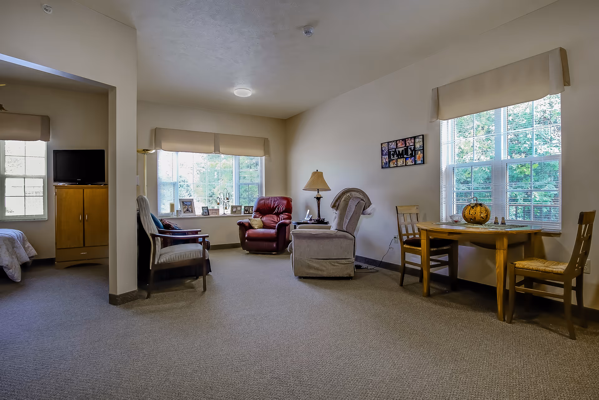 Bright common living room with chairs, table, pumpkin centerpiece, and large windows.