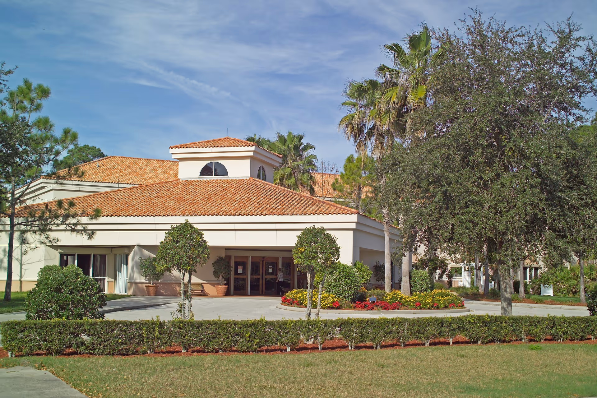 Exterior view of a Halifax Health Hospice building with a red-tiled roof and palm trees.