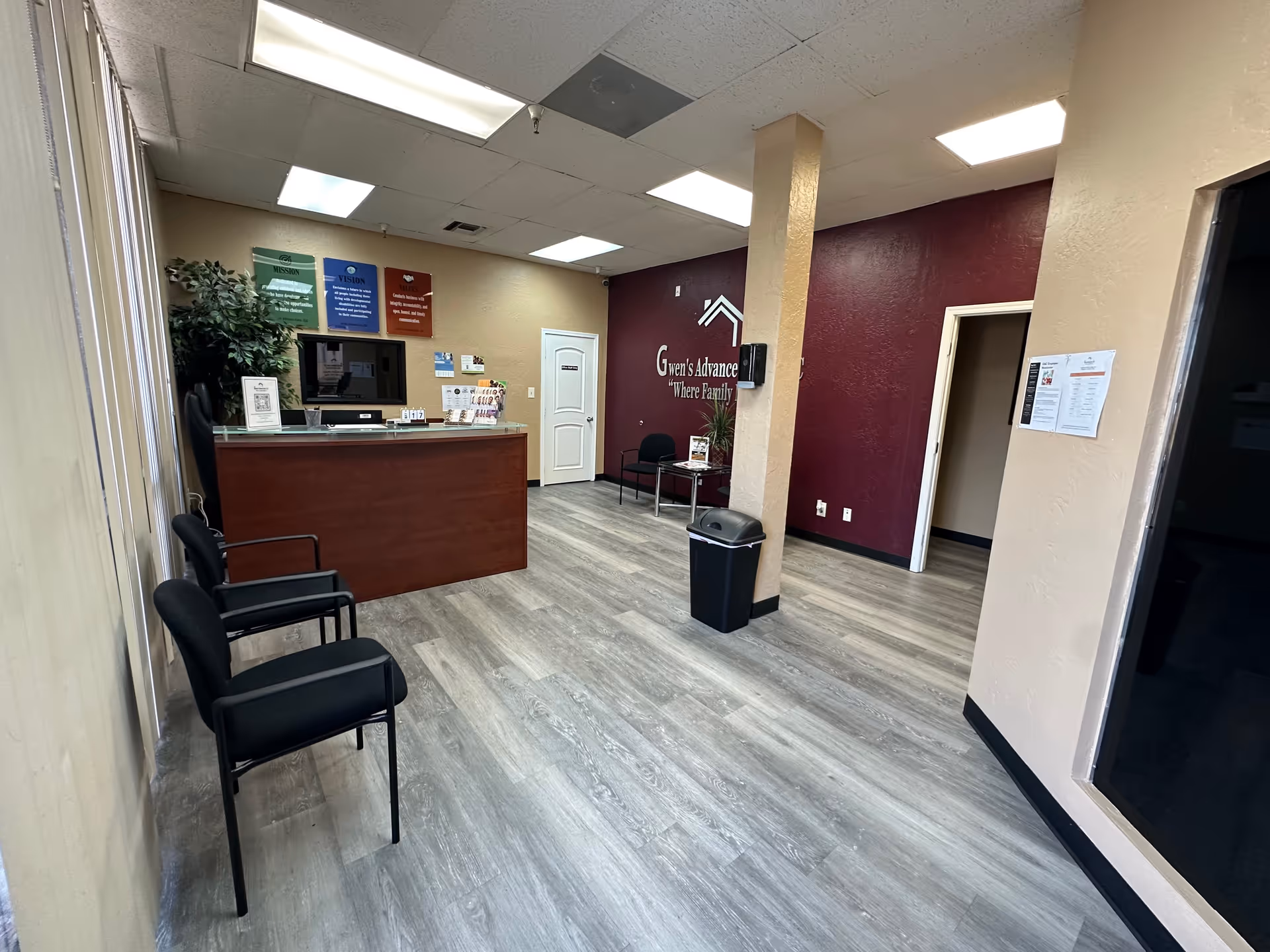 Interior reception lobby at Gwen's Advance Care with front desk, seating, and maroon wall.