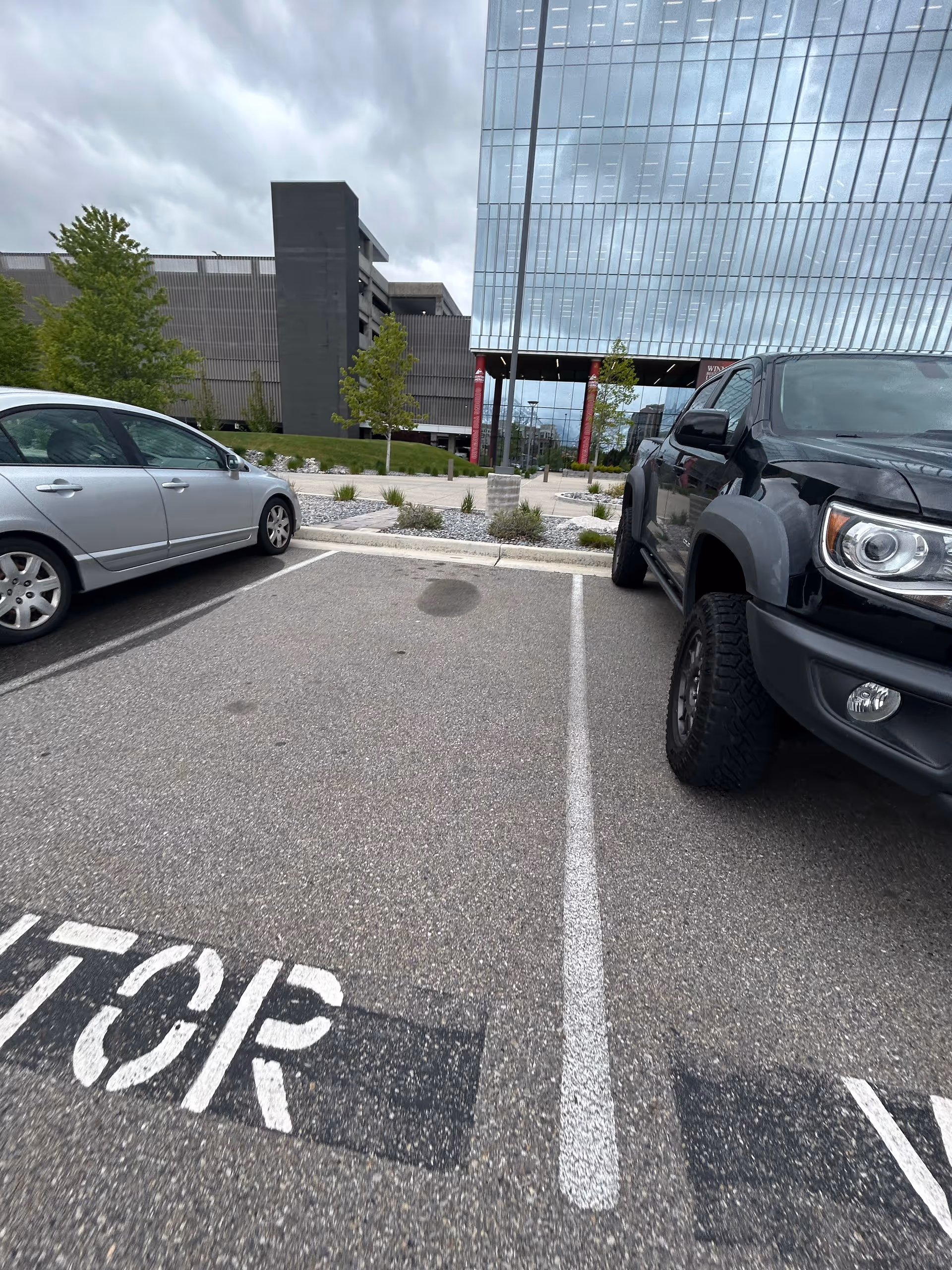 Parking lot beside a modern glass building entrance with two parked vehicles.