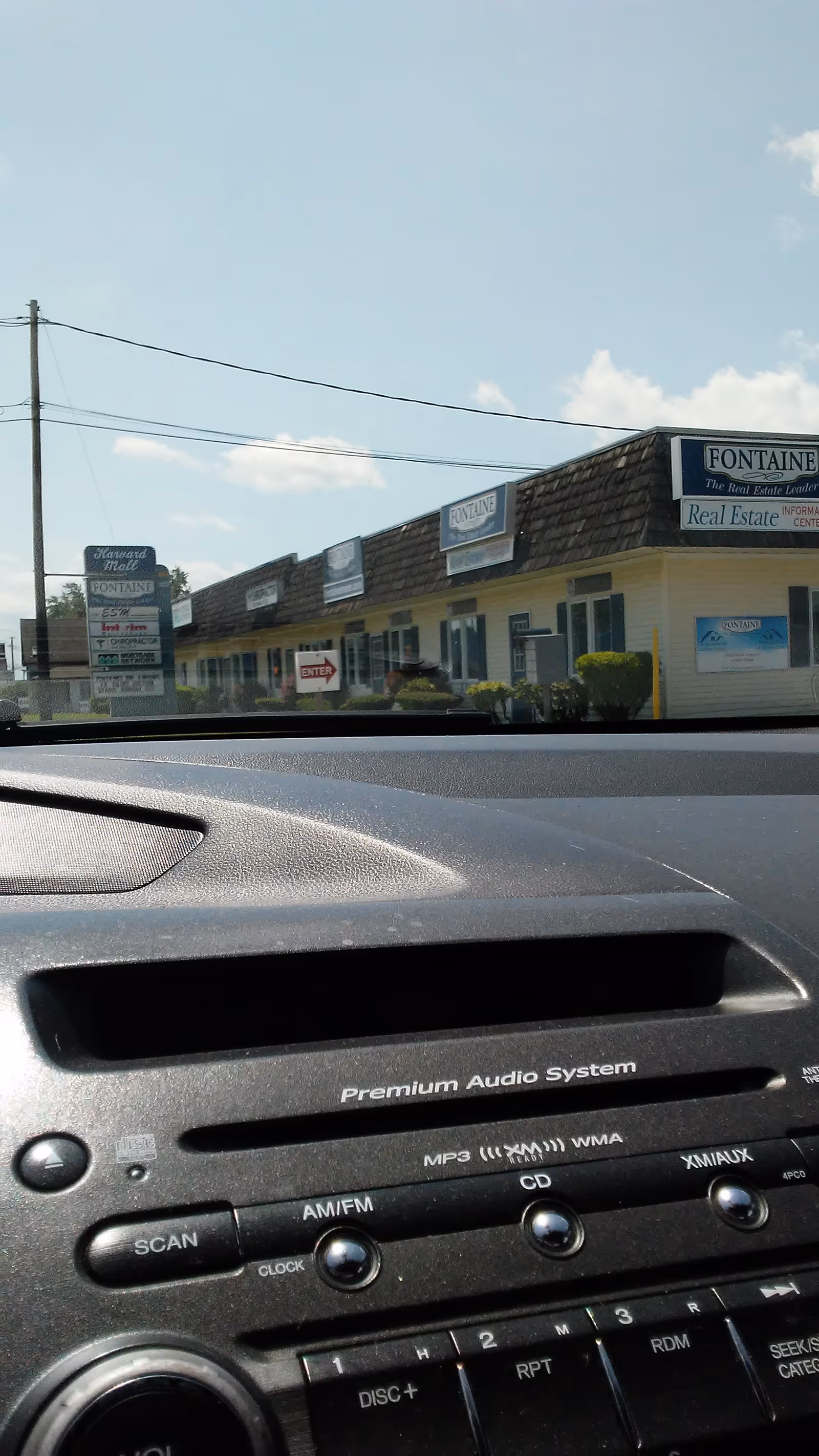 Dashboard view from inside a car looking at strip storefronts with Fontaine Real Estate signs.