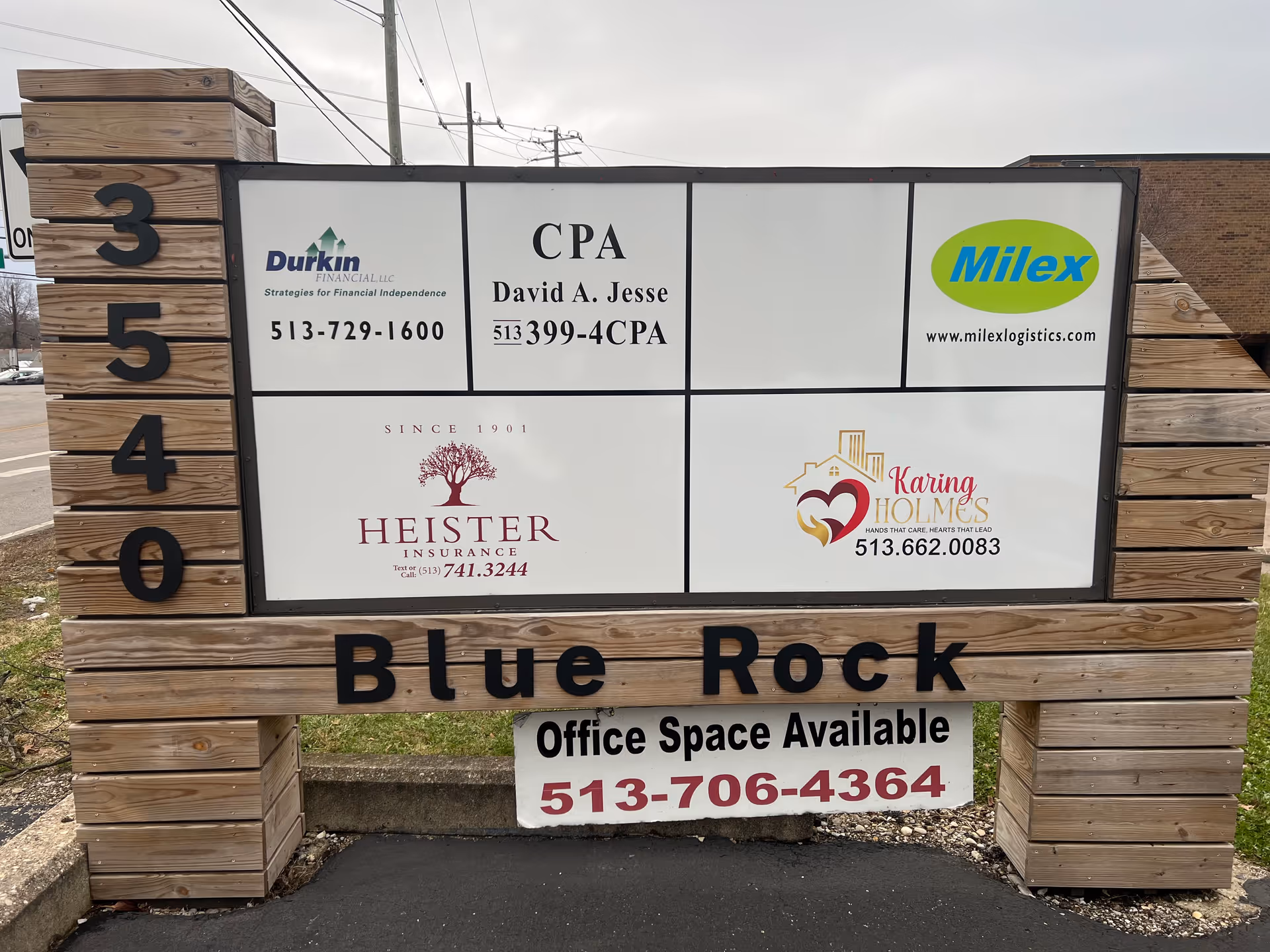 Outdoor wooden-framed signboard displays multiple logos and office space information.