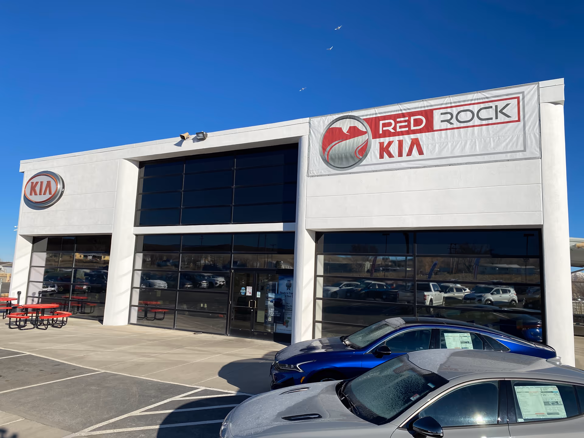 White Kia dealership building with Red Rock Kia sign and parked cars.