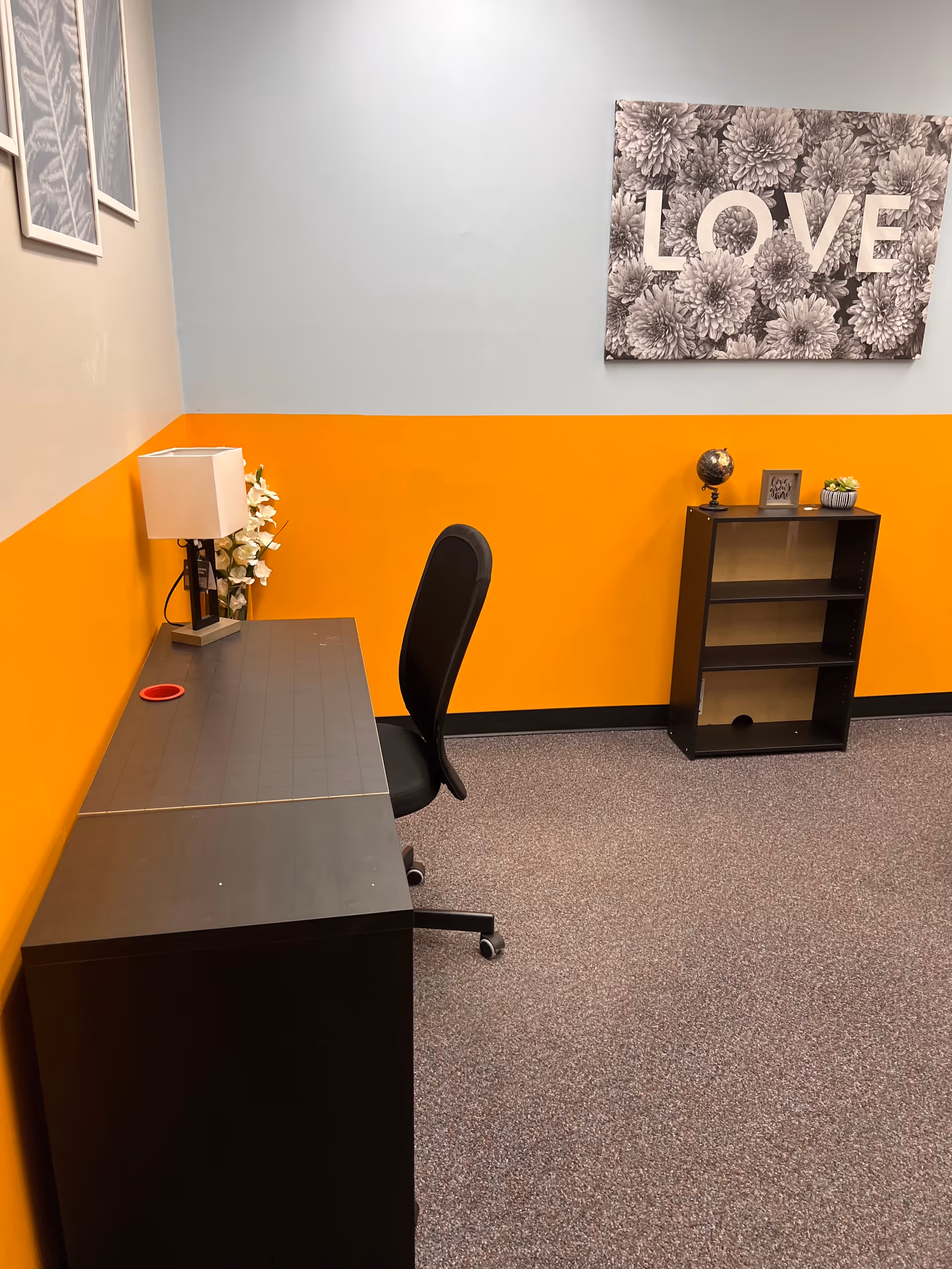 Office-style desk area with chair, lamp, orange wall and floral artwork.
