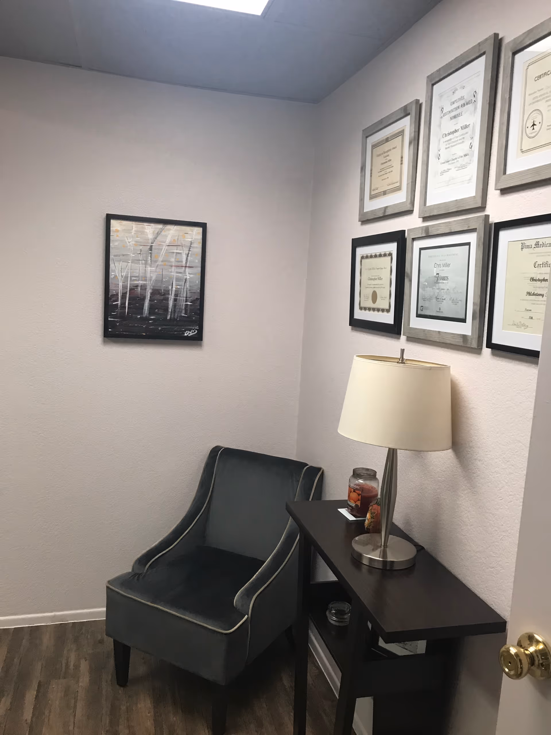 Corner office area with framed certificates, a lamp, and a padded chair.