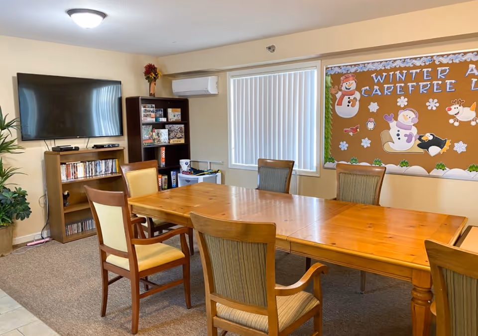 Interior dining area with long wooden table, chairs, TV, and bulletin board.