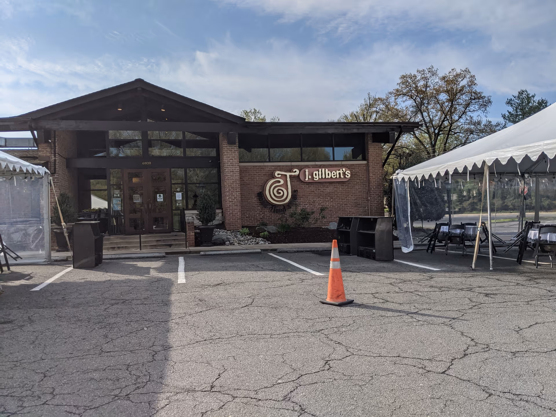 Brick building with glass doors and the J. Gilbert's sign, outdoor tents nearby.