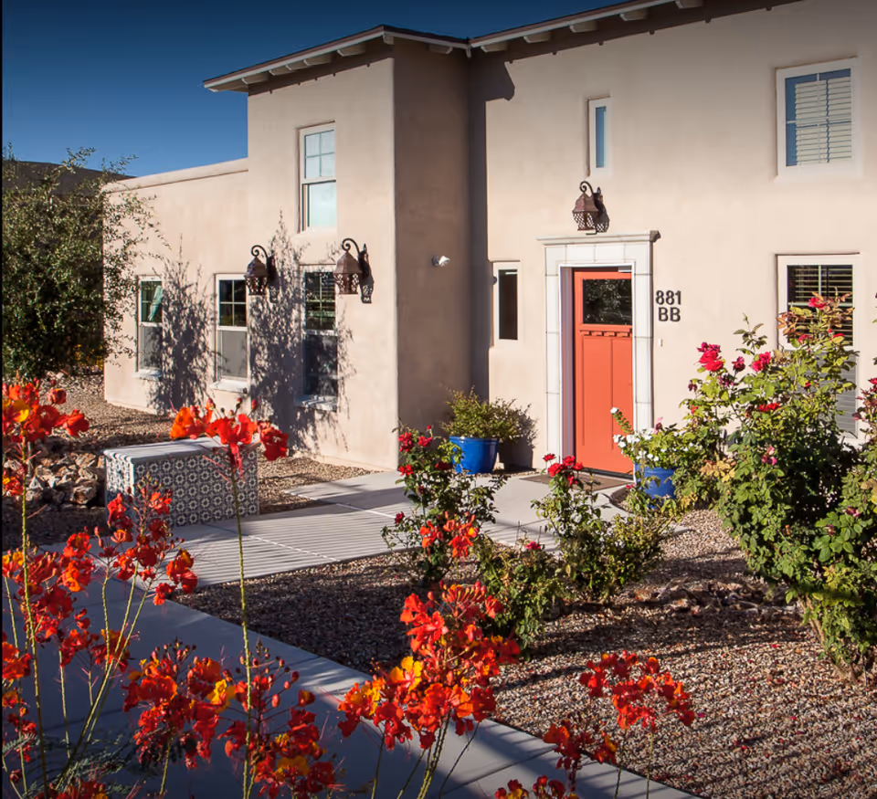 Exterior view of a senior living facility entrance with a red door and blooming flowers.