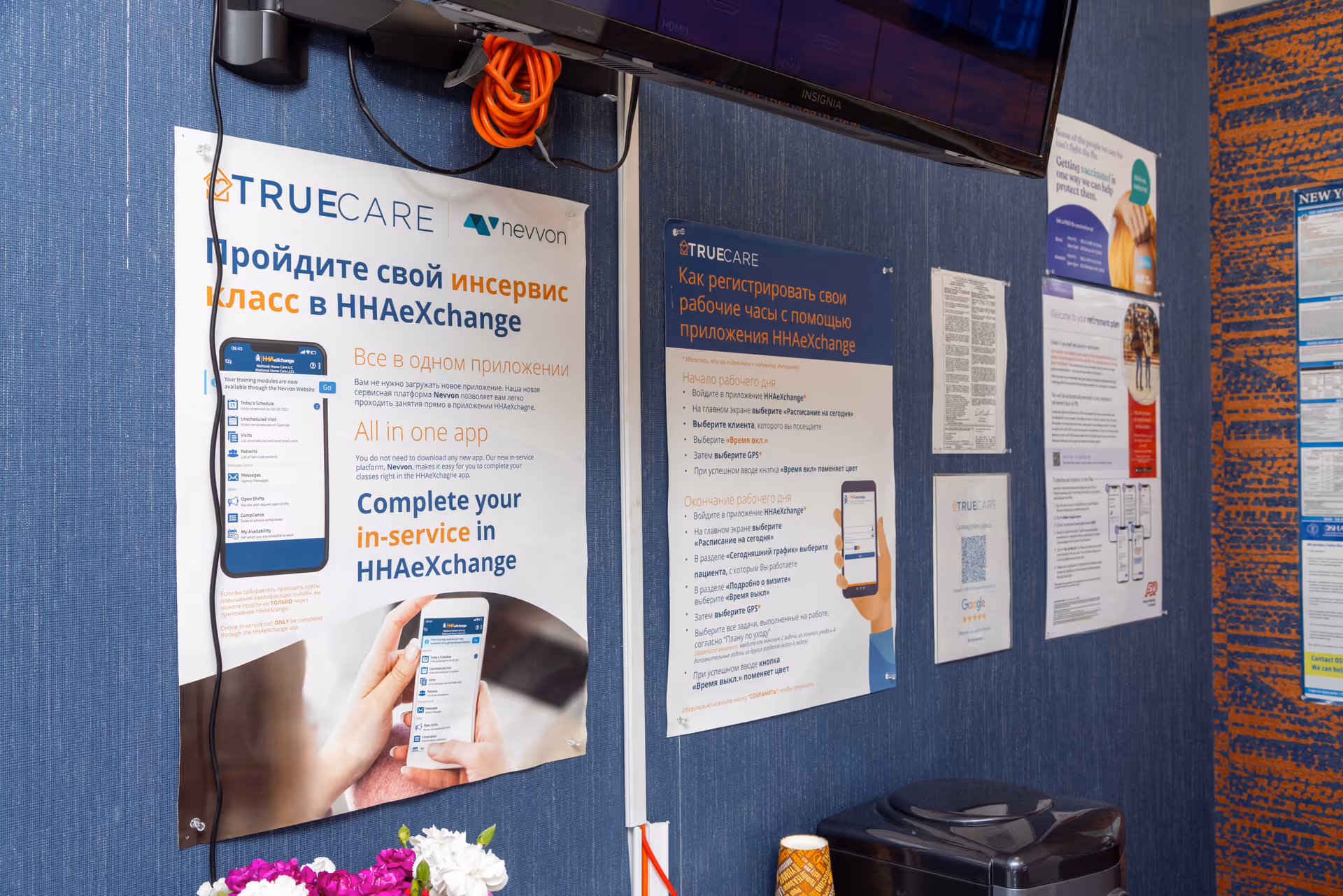 Indoor hallway with blue wall posters and a mounted TV in a senior care facility.