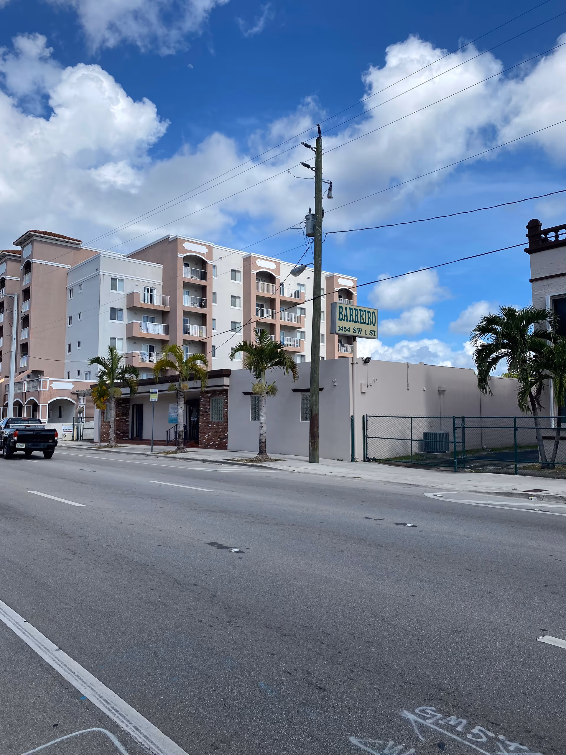 Street view of a multi-story beige building with palm trees and a Barreiro Enterprises sign