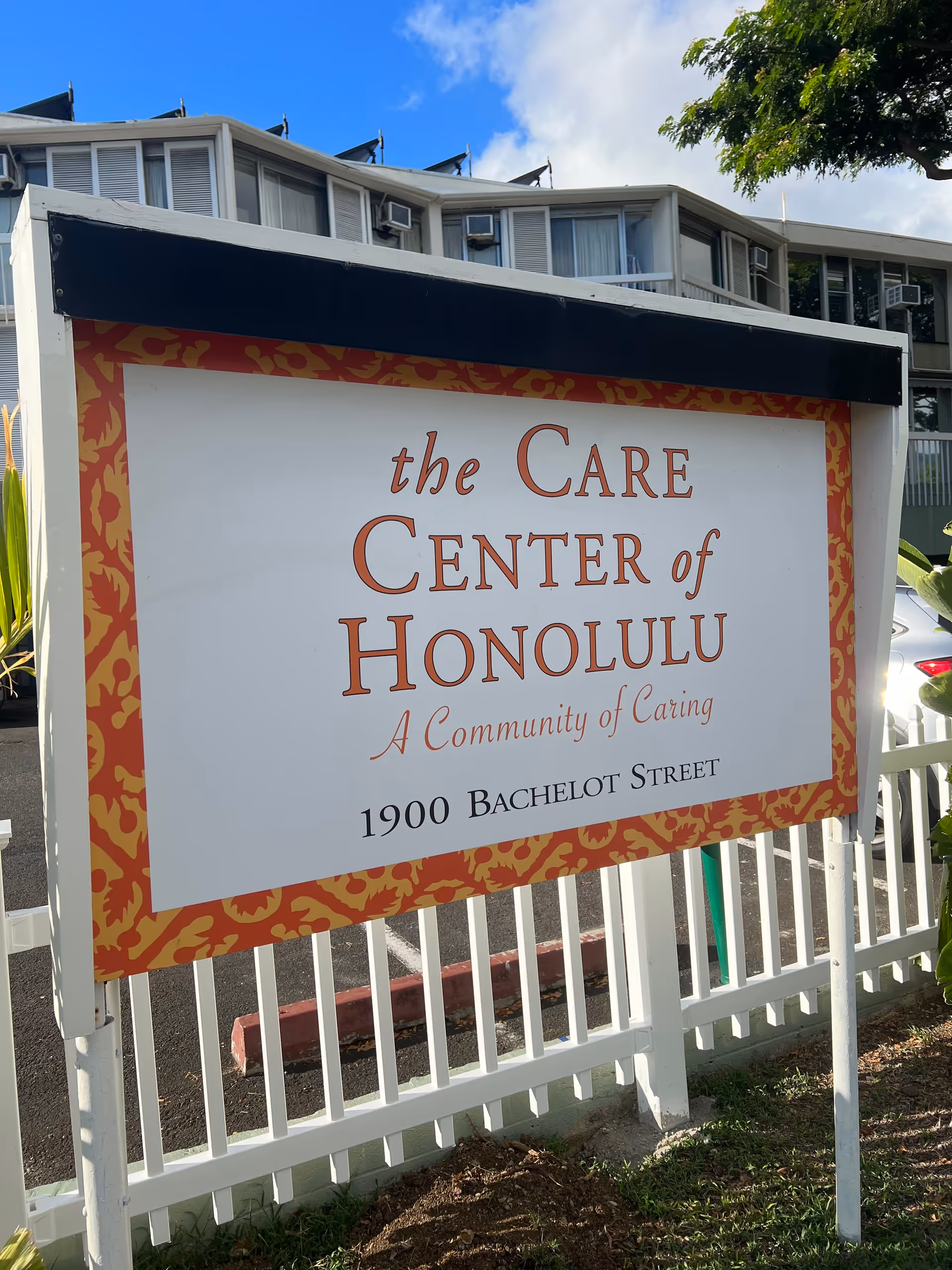 Outdoor sign reads The Care Center of Honolulu with a white fence and building behind.