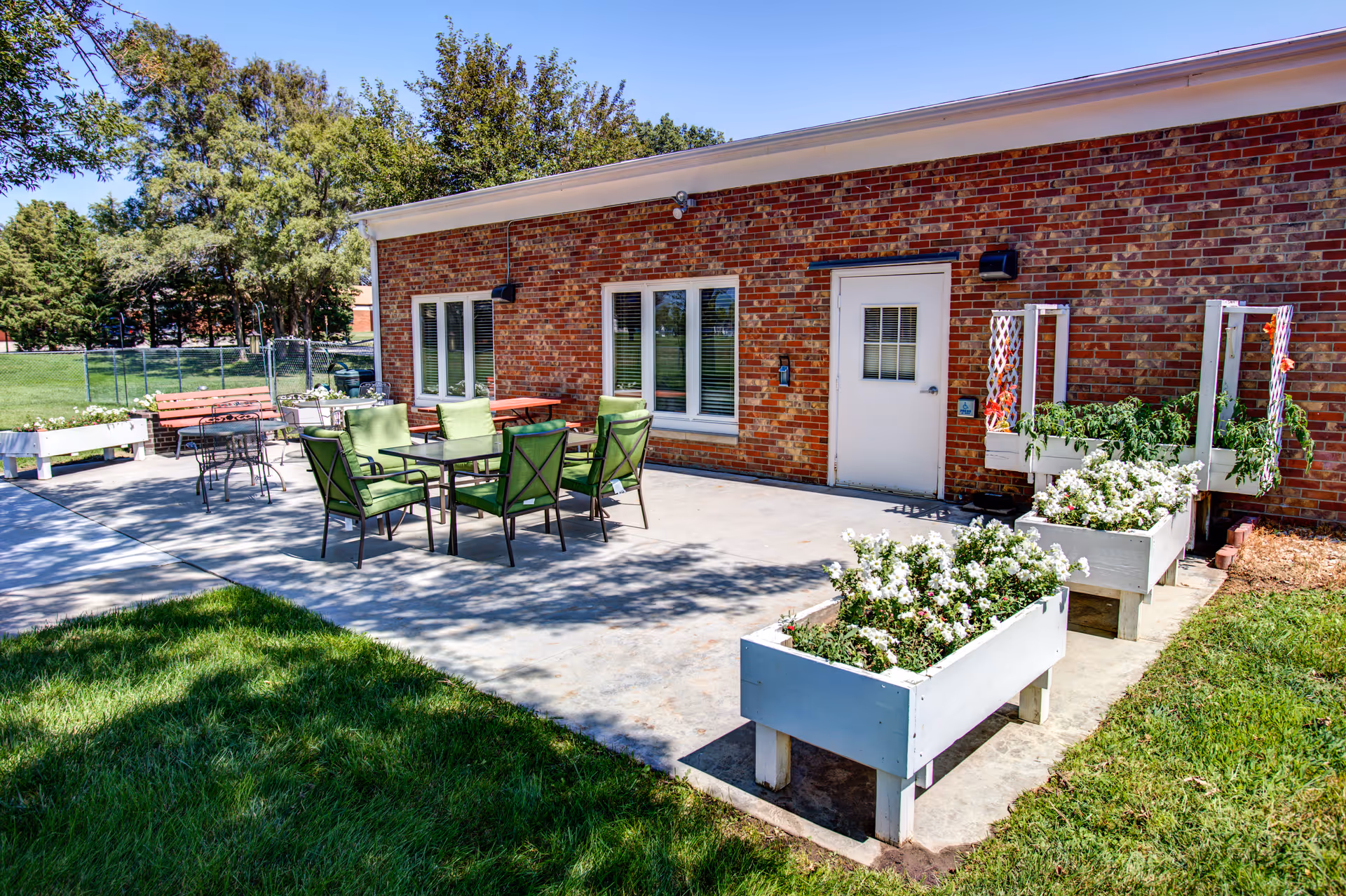 Brick building with outdoor patio, green chairs, tables, and white flowering planters.