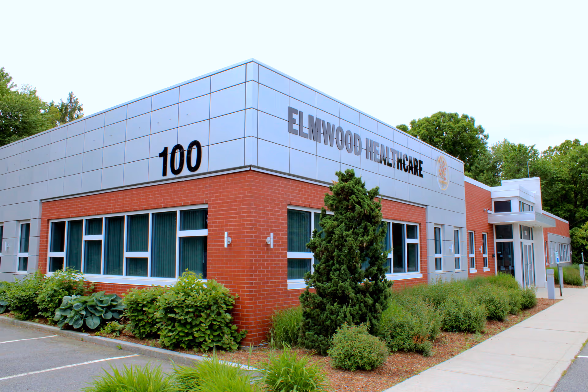 Exterior view of Elmwood Healthcare building with red brick, metal siding, and landscaping.