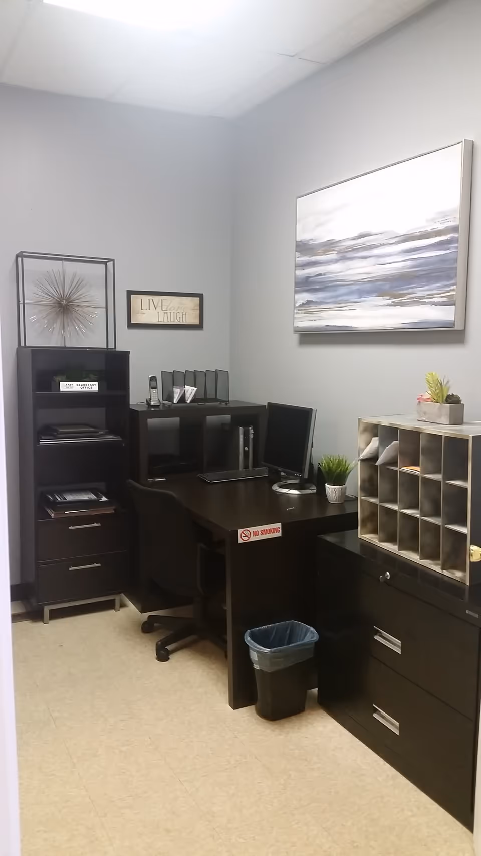 Dark wooden office desk with computer and filing cabinets in a small, organized office.