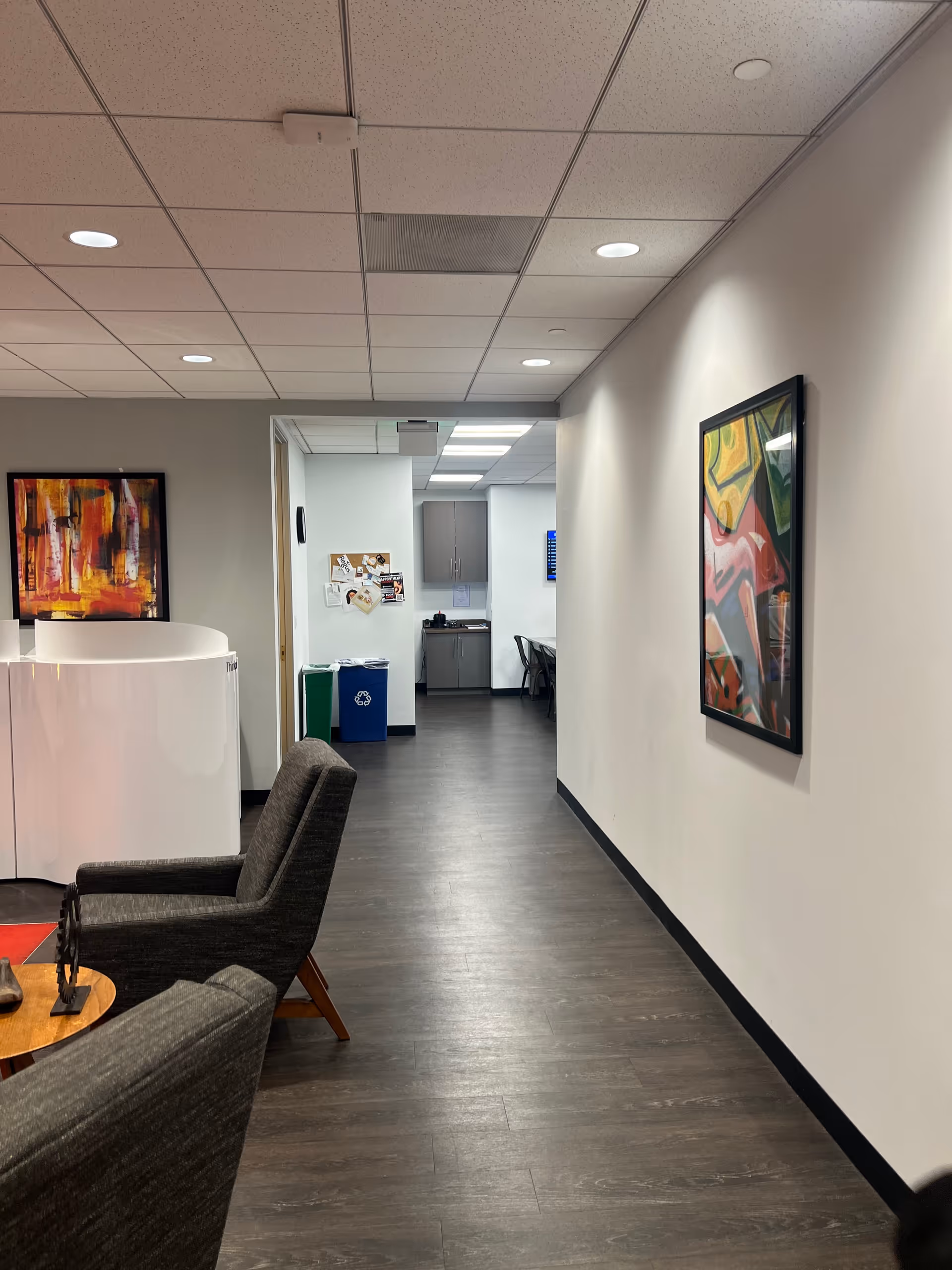 Indoor hallway of a senior living facility with seating, artwork, and a kitchenette area.
