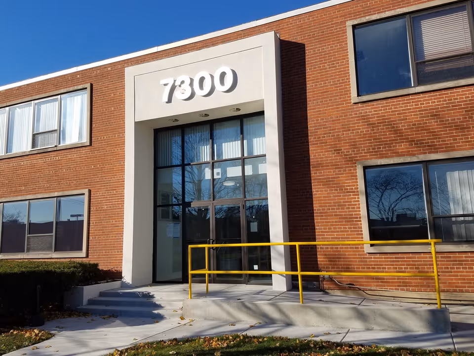 Exterior view of a brick building entrance with stairs and a yellow ramp.