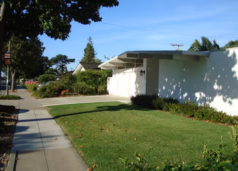 Exterior of a white senior living facility with a sidewalk and green lawn.