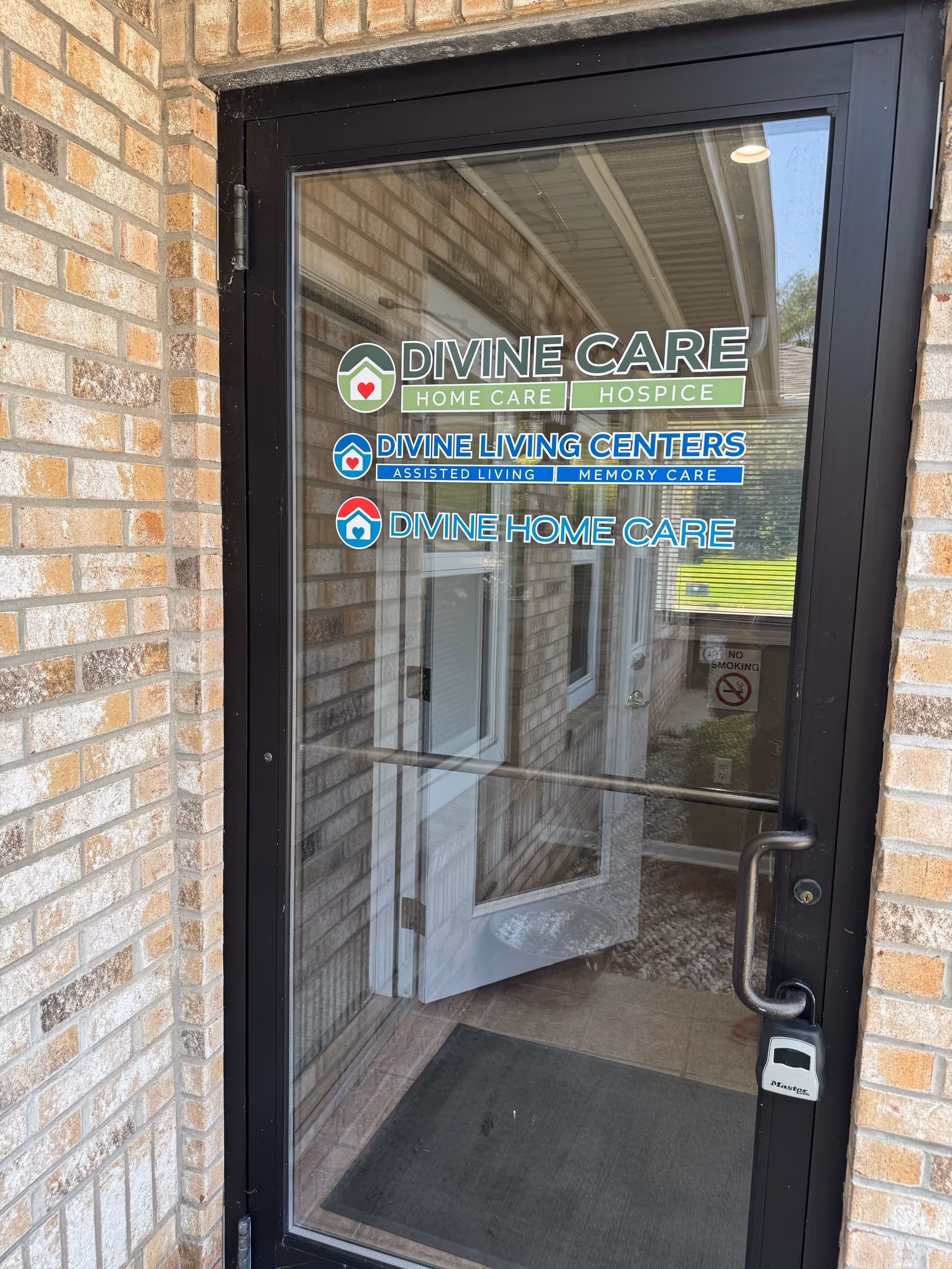 Glass door with Divine Care branding and signage on brick building exterior.