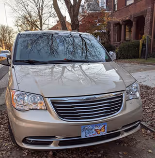 Front view of a beige minivan parked on a residential street near a brick building.