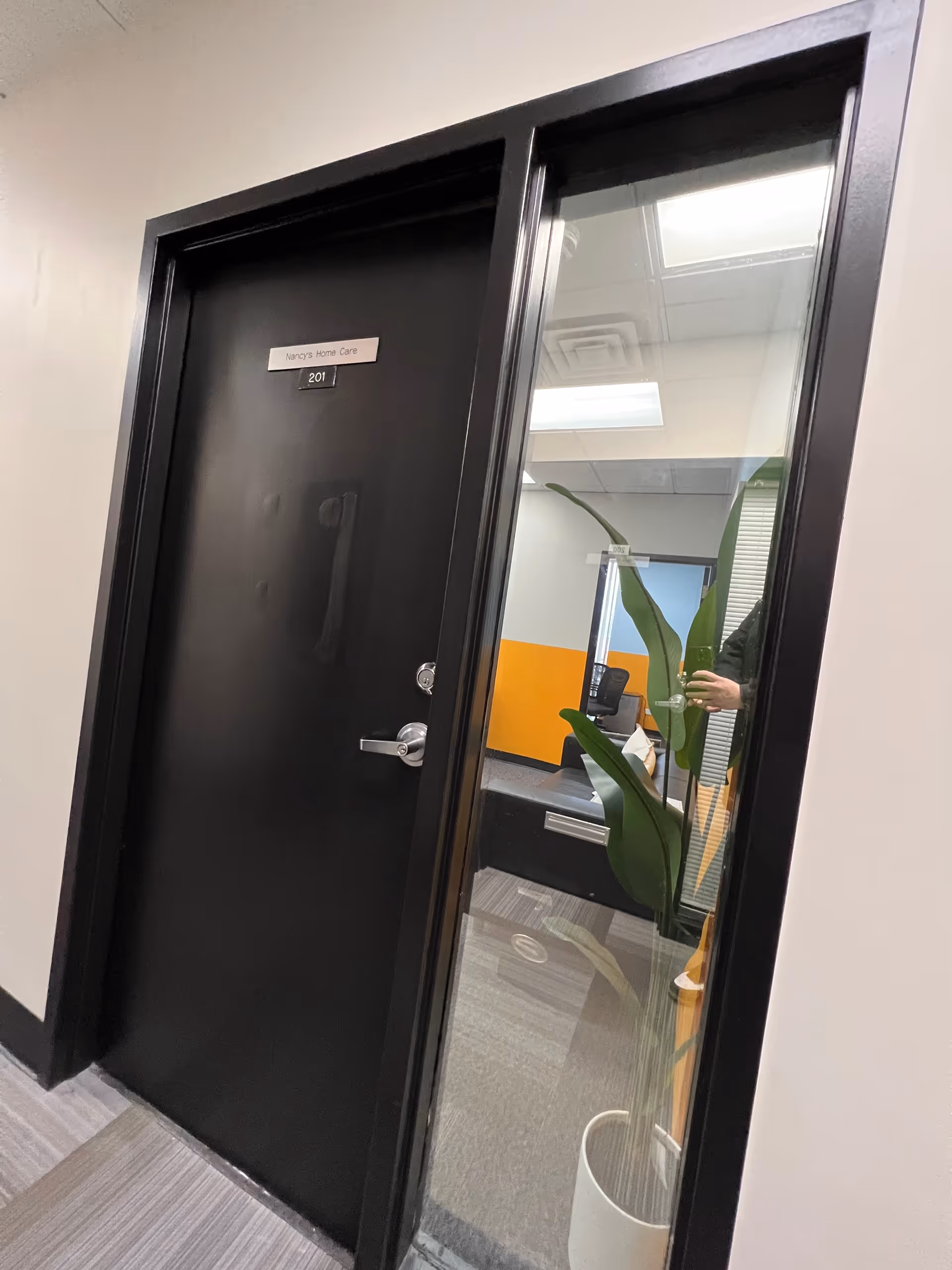 Interior hallway with a black door labeled Nancy's Home Care and glass panel with a plant.
