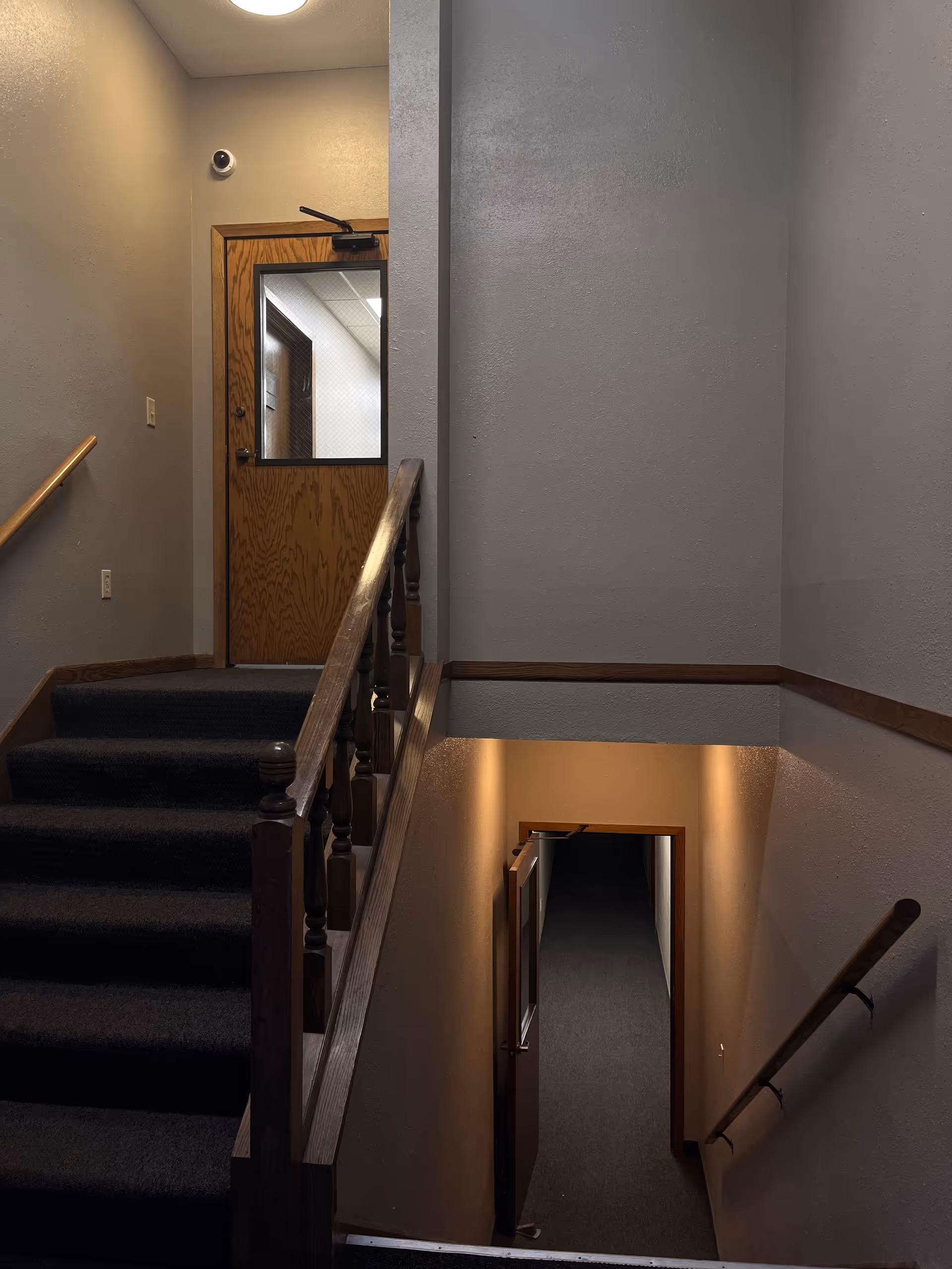 Interior stairwell with wooden railing and landing, dim lighting, leading to a door.