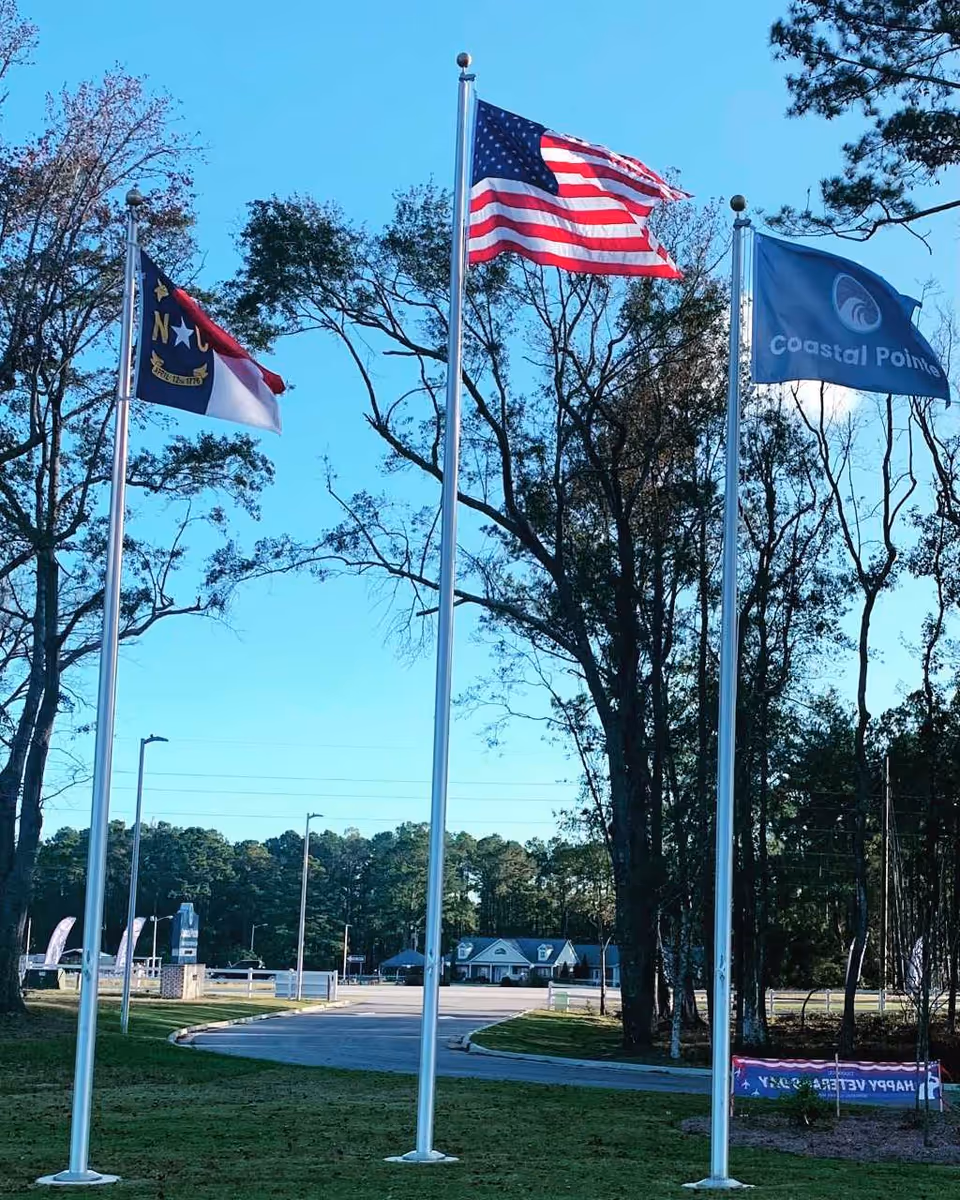 Three flagpoles with American and state flags in front of Coastal Pointe.