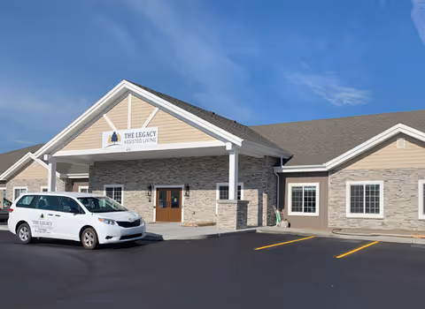 Front exterior of The Legacy Assisted Living building with a parked white van.