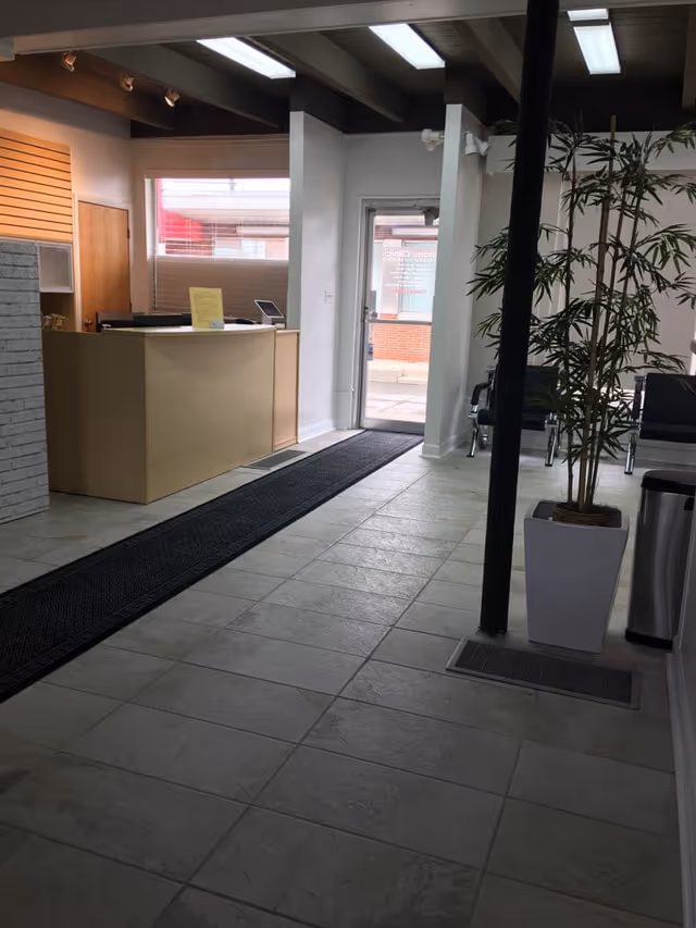 Facility lobby with curved reception desk, tiled floor, seating area, and tall potted plant.
