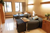 Two beds in a bright, tidy shared room with window view and furnishings.