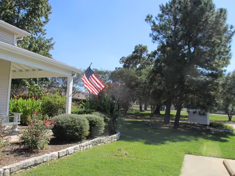 Exterior of Heritage Park Village showing a porch, American flag, shrubs, and a green lawn.