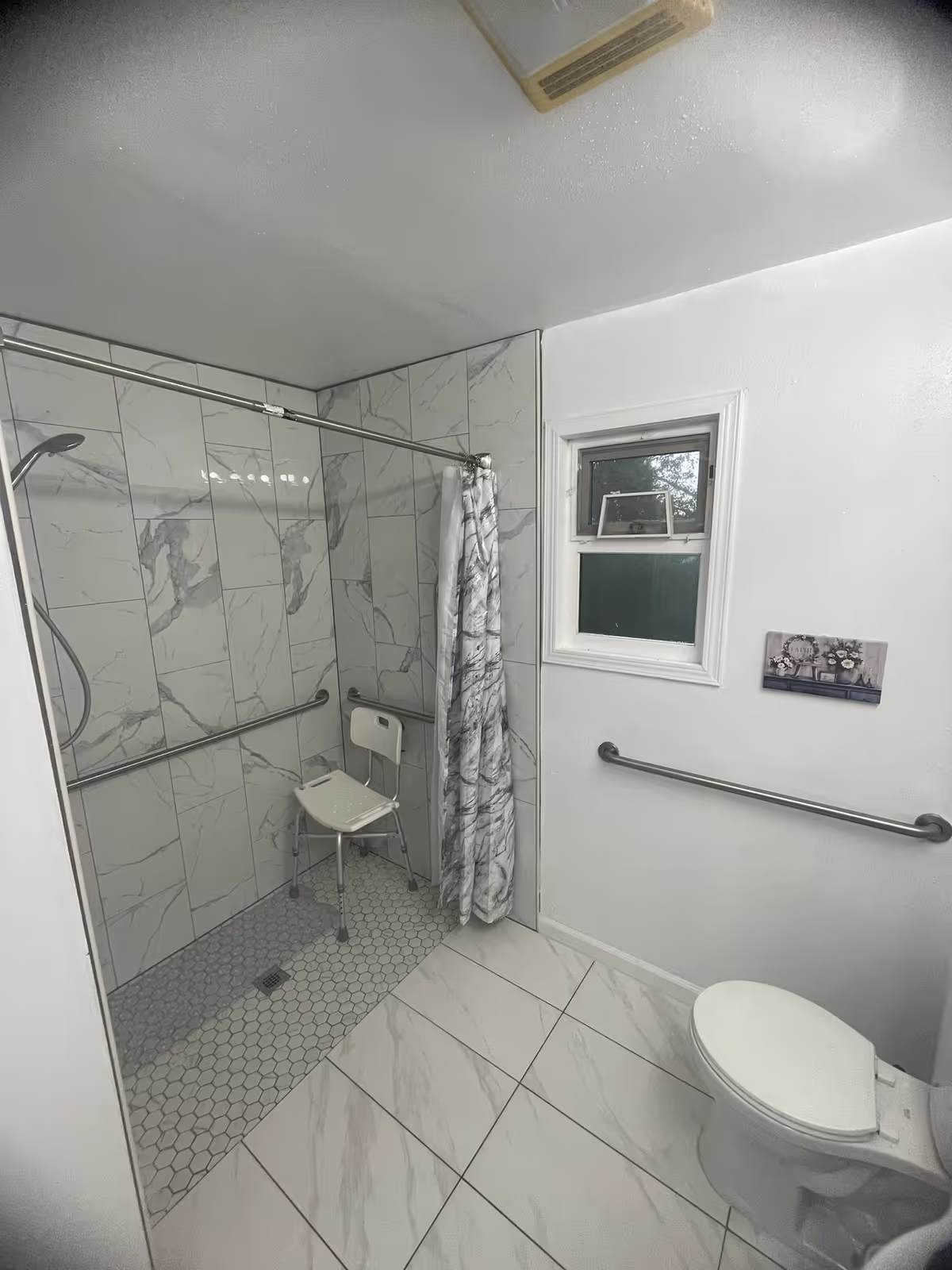 Accessible bathroom with tiled shower, shower chair, grab bars, and a toilet.