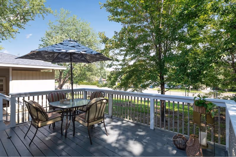 Outdoor deck at Bright Path Homes with table, chairs, umbrella, and surrounding trees.